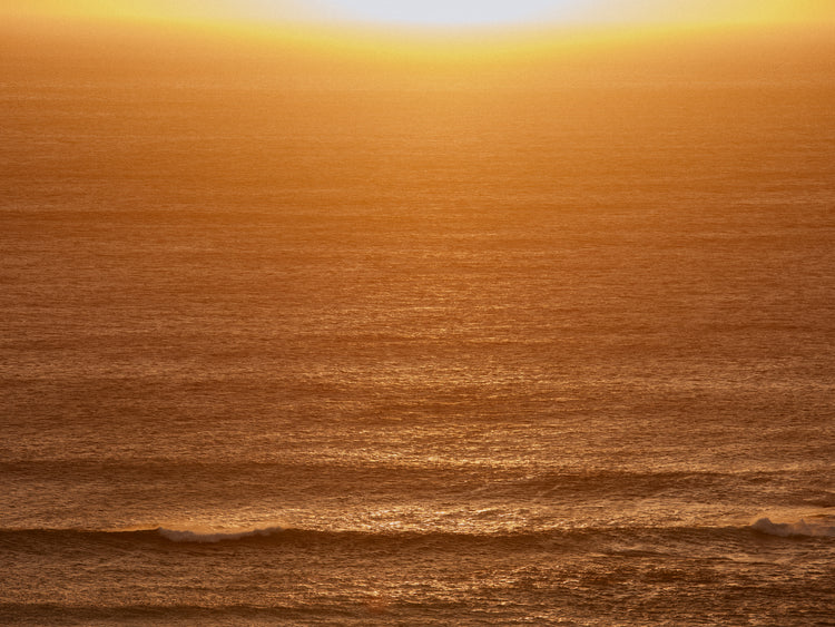 Sun setting over the ocean coloring the water in orange and yellow.