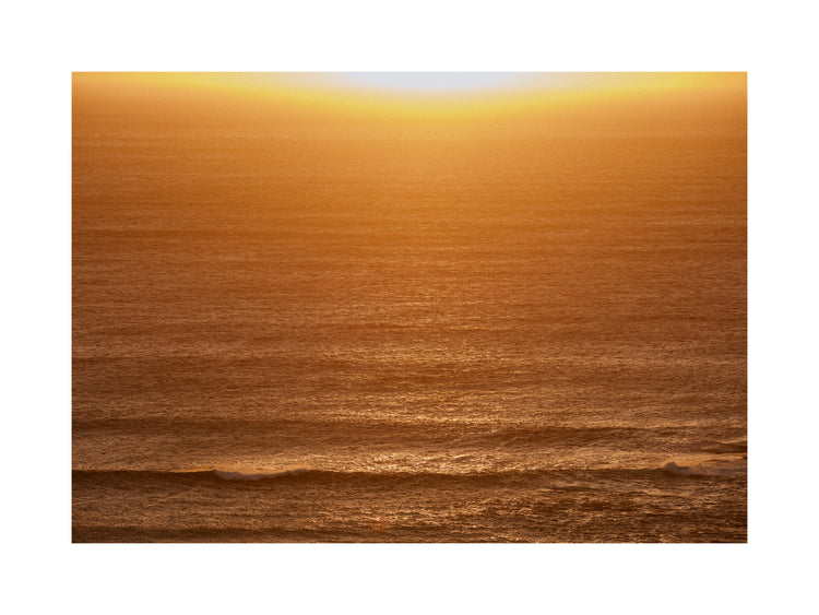 Sun setting over the ocean coloring the water in orange and yellow.
