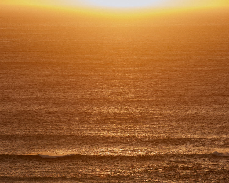Sun setting over the ocean coloring the water in orange and yellow.