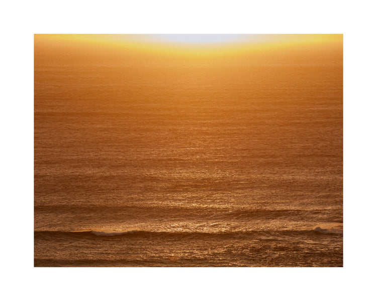 Sun setting over the ocean coloring the water in orange and yellow.