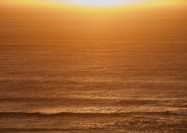 Sun setting over the ocean coloring the water in orange and yellow.