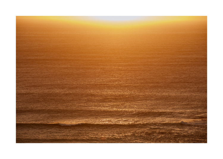 Sun setting over the ocean coloring the water in orange and yellow.