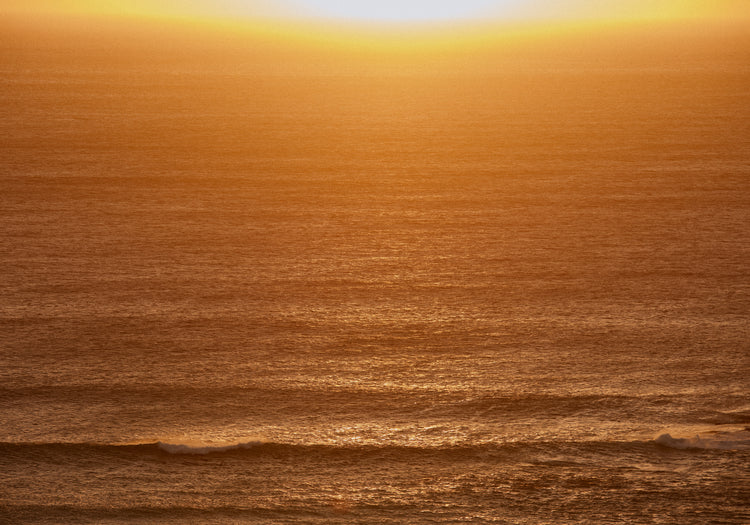 Sun setting over the ocean coloring the water in orange and yellow.