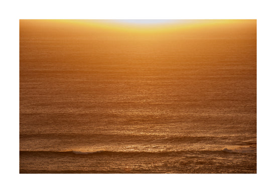 Sun setting over the ocean coloring the water in orange and yellow.