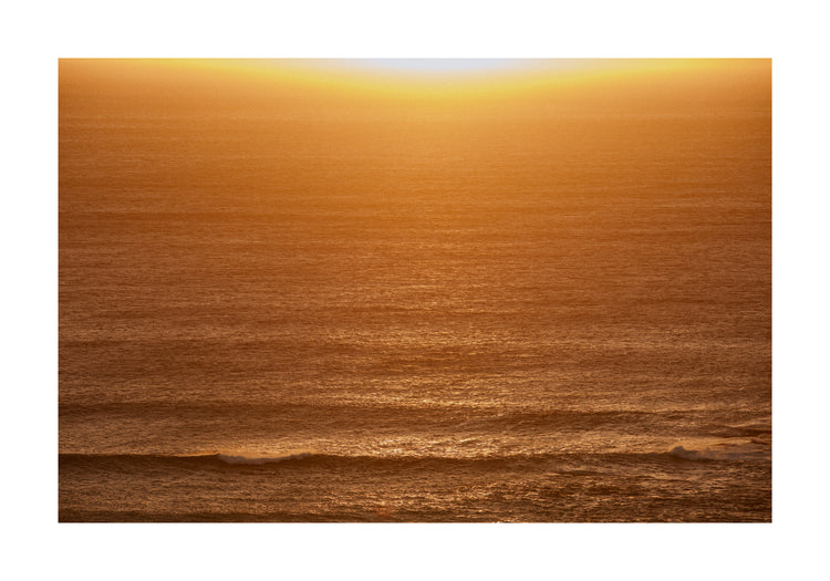 Sun setting over the ocean coloring the water in orange and yellow.