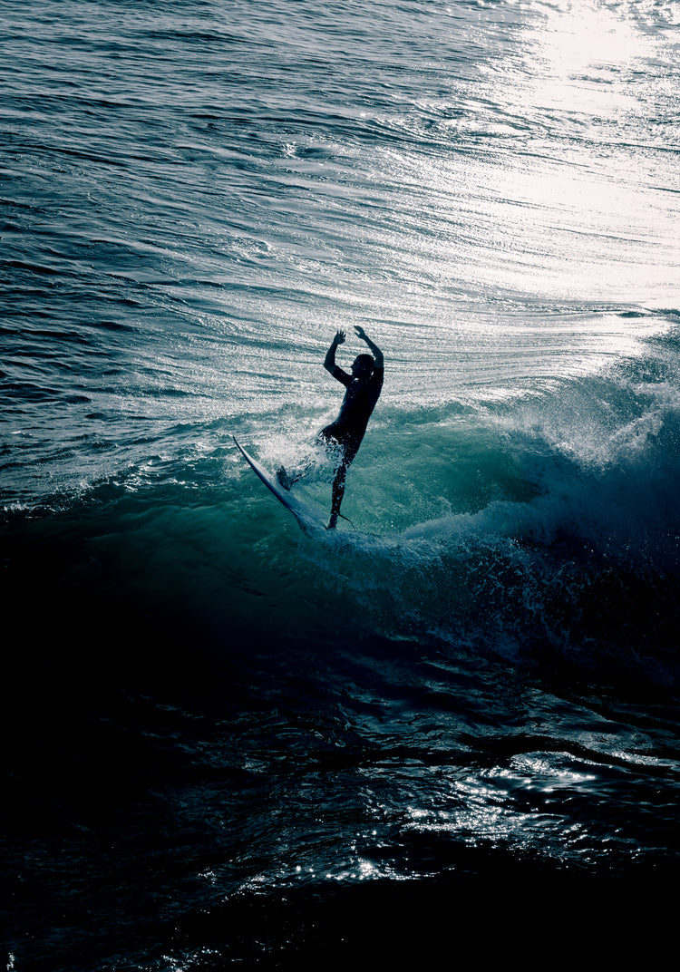 Man surfing a right-hander wave one a blue ocean reflecting white in the sun.