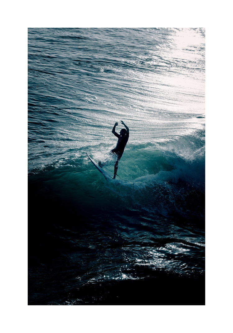 Man surfing a right-hander wave one a blue ocean reflecting white in the sun.