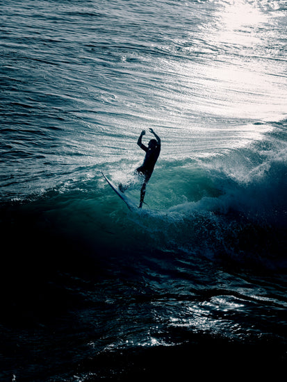 Man surfing a right-hander wave one a blue ocean reflecting white in the sun.