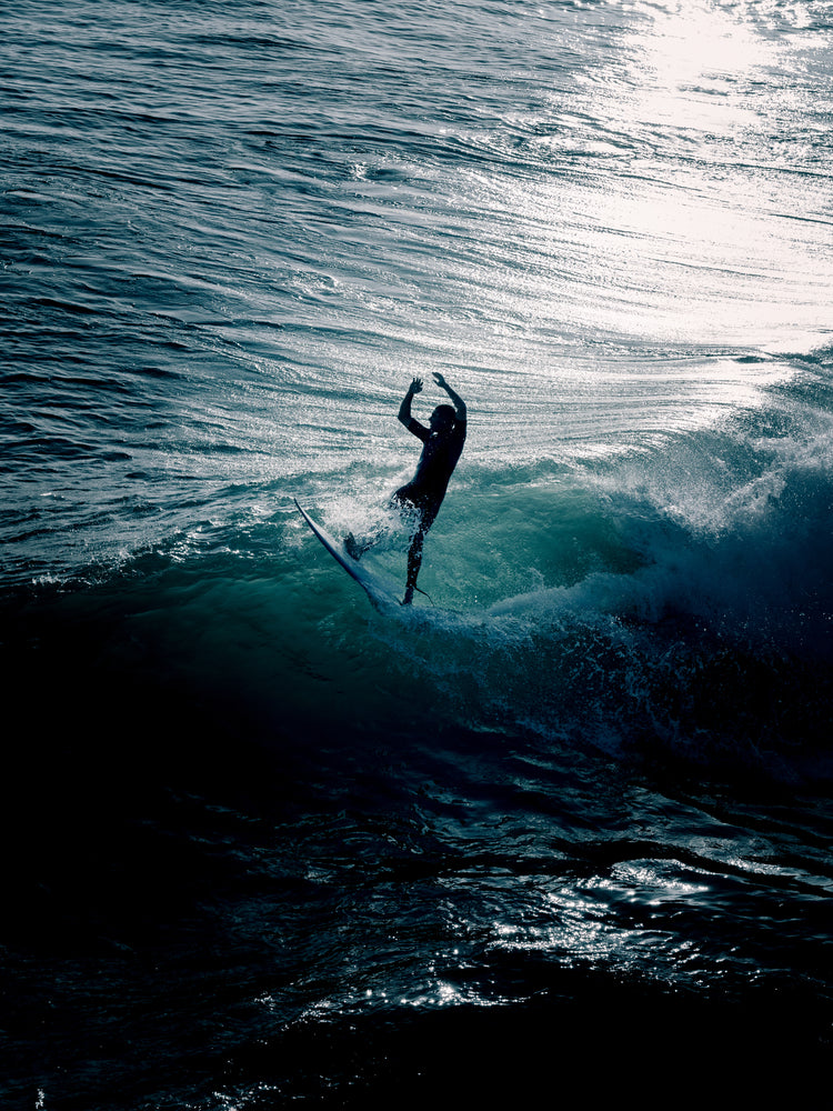 Man surfing a right-hander wave one a blue ocean reflecting white in the sun.