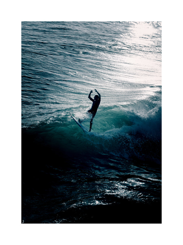 Man surfing a right-hander wave one a blue ocean reflecting white in the sun.
