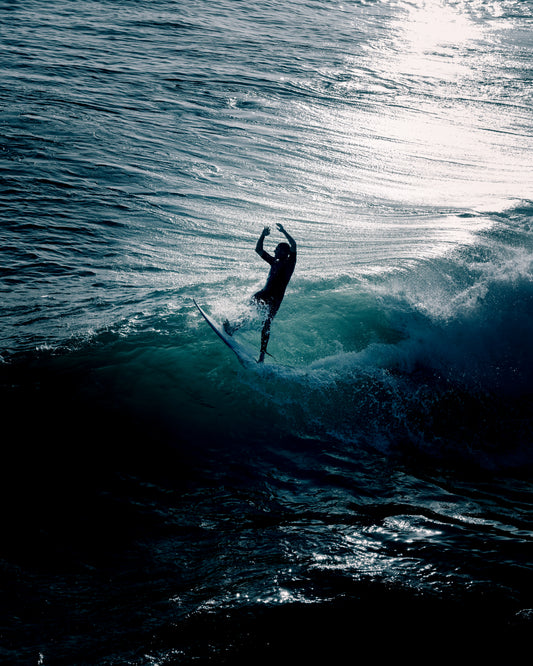 Man surfing a right-hander wave one a blue ocean reflecting white in the sun.