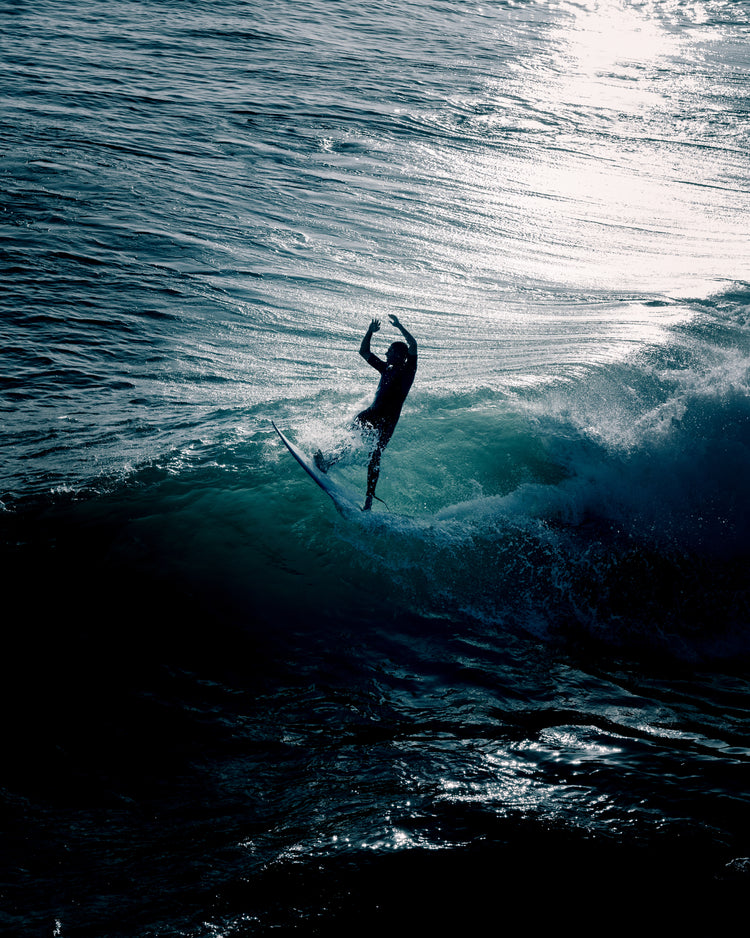 Man surfing a right-hander wave one a blue ocean reflecting white in the sun.