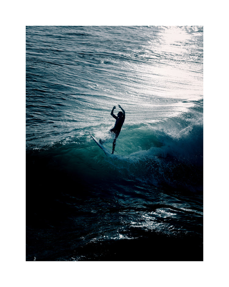 Man surfing a right-hander wave one a blue ocean reflecting white in the sun.