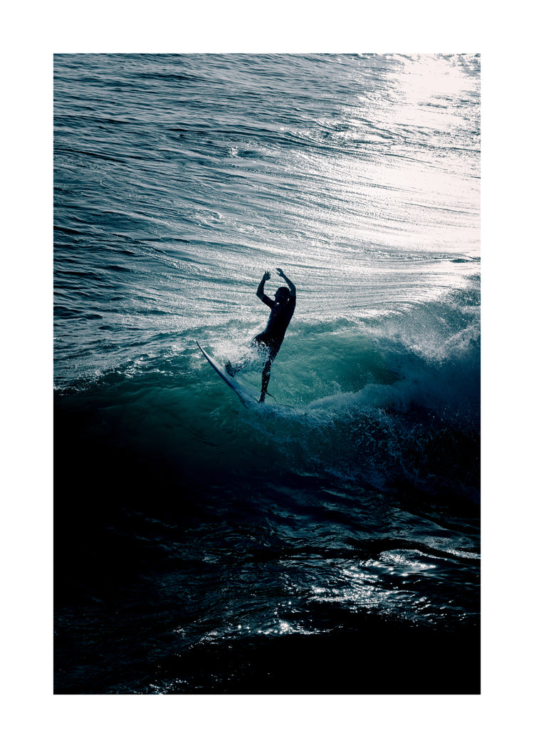 Man surfing a right-hander wave one a blue ocean reflecting white in the sun.