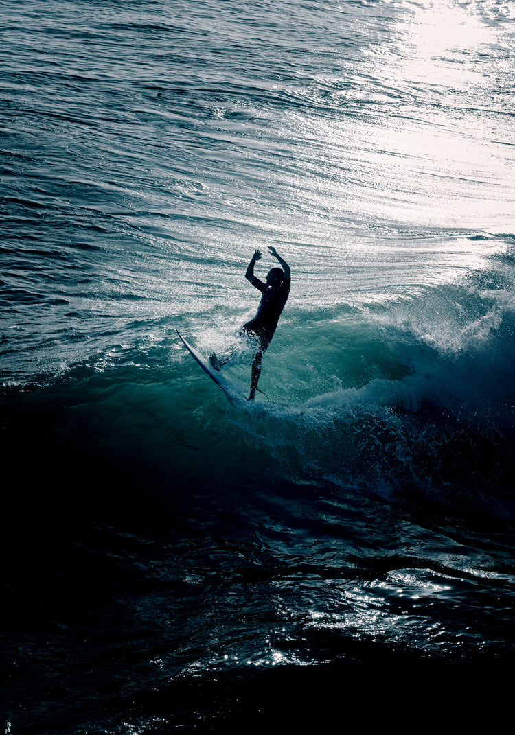 Man surfing a right-hander wave one a blue ocean reflecting white in the sun.