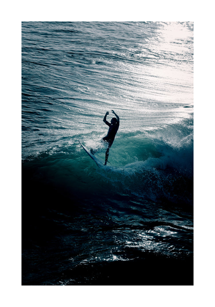 Man surfing a right-hander wave one a blue ocean reflecting white in the sun.