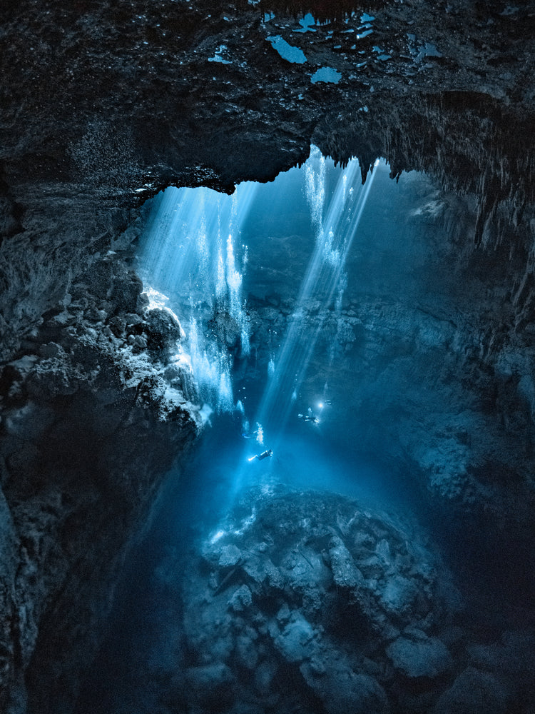 Divers exploring a deep blue water cave.
