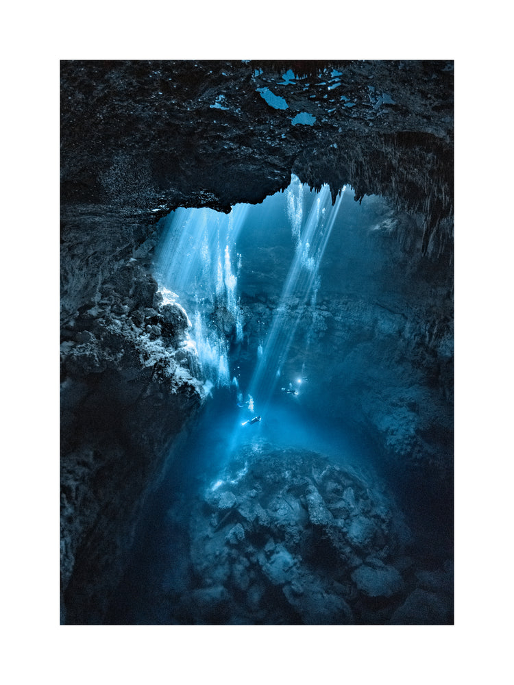 Divers exploring a deep blue water cave.
