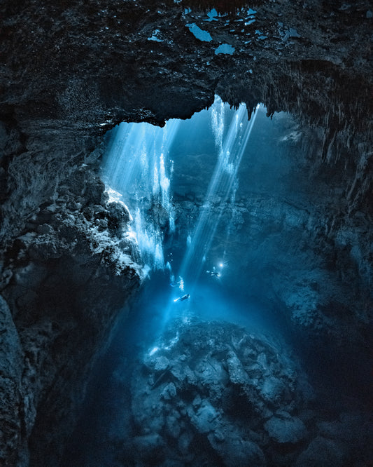 Divers exploring a deep blue water cave.