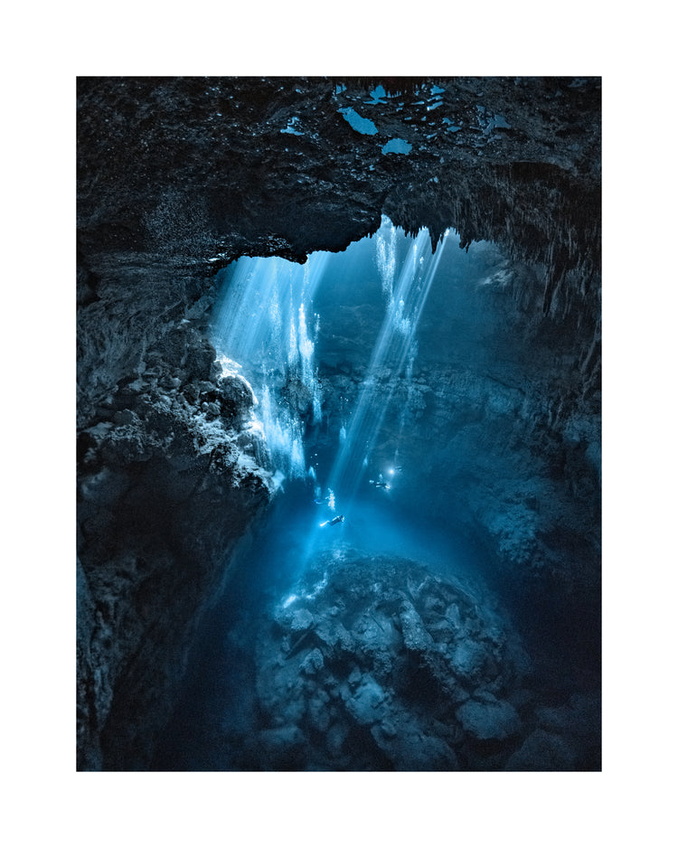 Divers exploring a deep blue water cave.