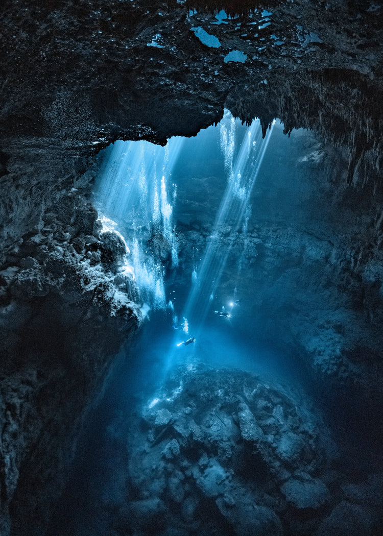Divers exploring a deep blue water cave.
