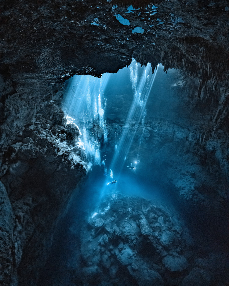 Divers exploring a deep blue water cave.