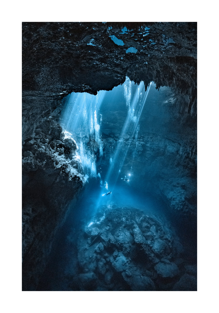 Divers exploring a deep blue water cave.