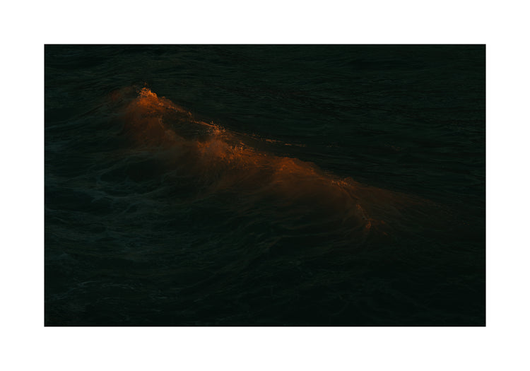 Waves colored orange from the setting sun in the ocean.
