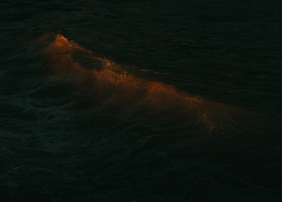 Waves colored orange from the setting sun in the ocean.