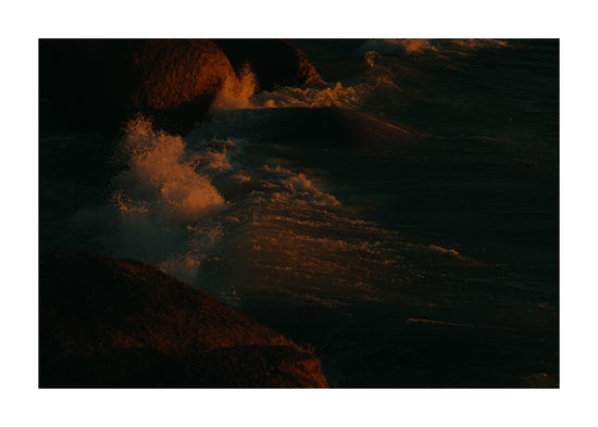 Waves crashing into the cliffs at shore during sunset.