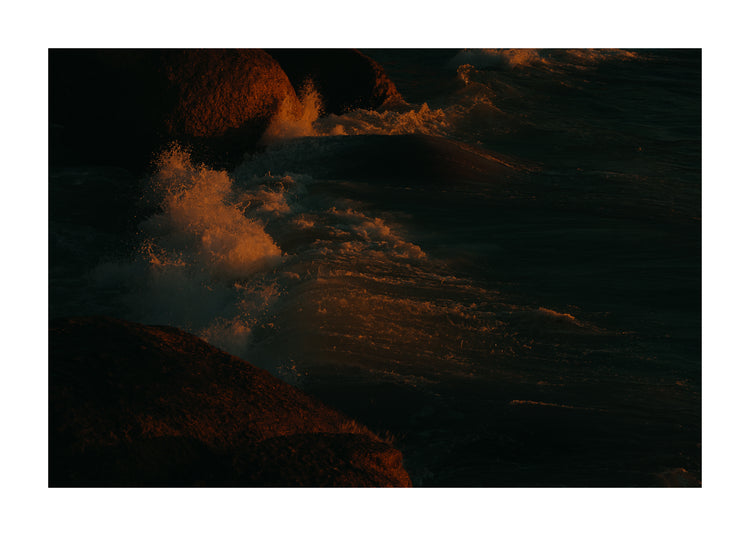 Waves crashing into the cliffs at shore during sunset.