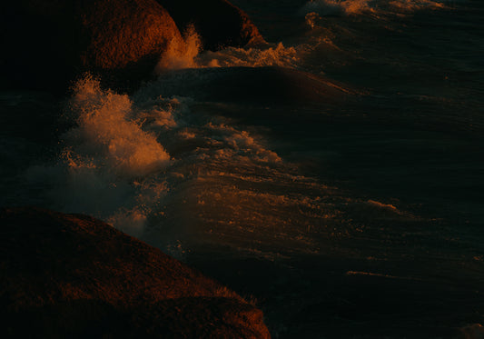 Waves crashing into the cliffs at shore during sunset.