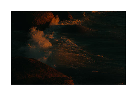 Waves crashing into the cliffs at shore during sunset.