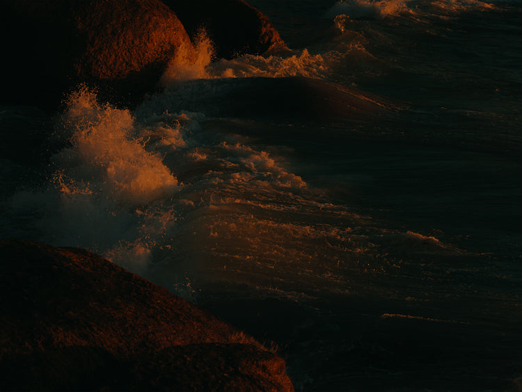 Waves crashing into the cliffs at shore during sunset.