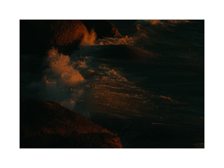 Waves crashing into the cliffs at shore during sunset.