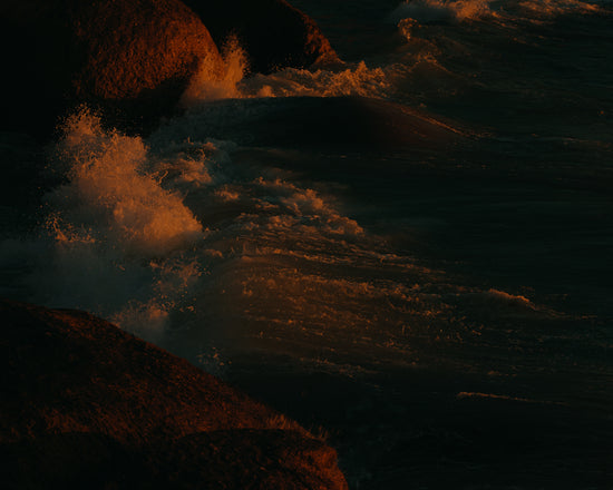 Waves crashing into the cliffs at shore during sunset.