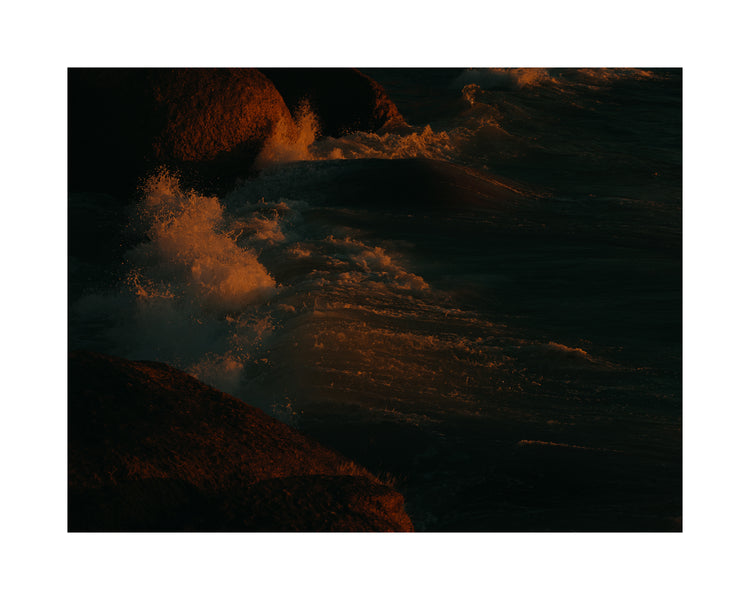 Waves crashing into the cliffs at shore during sunset.