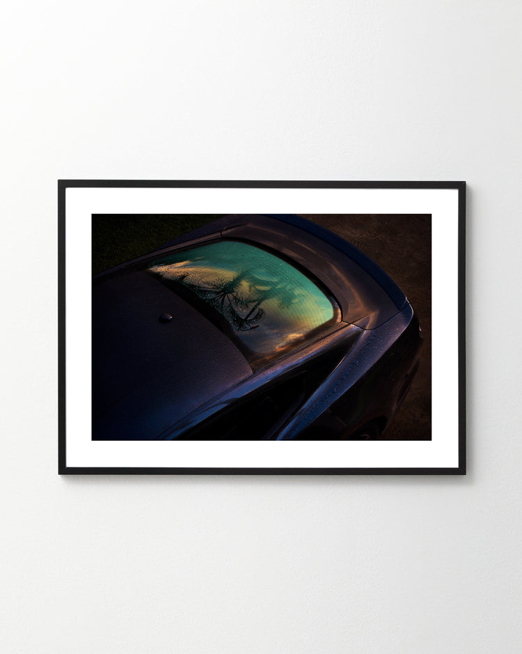 The Gas Up Poster captures a sleek car with dew on the windshield under a vibrant sky, embodying pedal to the metal. Displayed on a plain white wall and viewed from an elevated angle, it highlights dynamic presence.