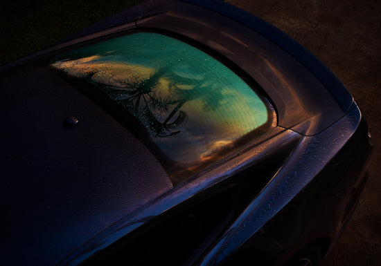 Sunset sky and outlines of palm trees reflected in a rain-stained car window.