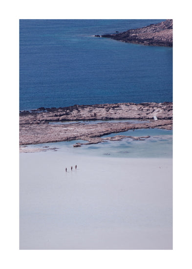 Three people walking in the shallows, heading towards the deep blue ocean ahead.