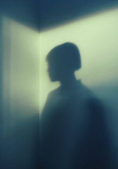 Shadow of a woman with short hair in the corner of a room with white walls.