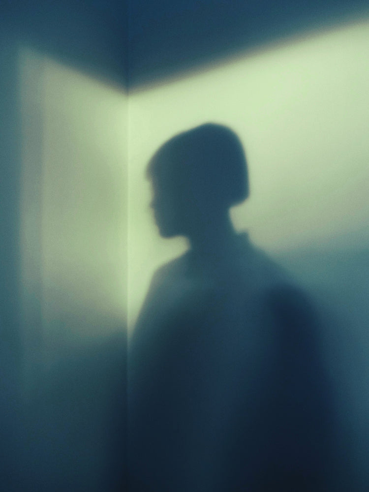 Shadow of a woman with short hair in the corner of a room with white walls.