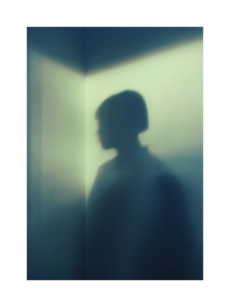 Shadow of a woman with short hair in the corner of a room with white walls.