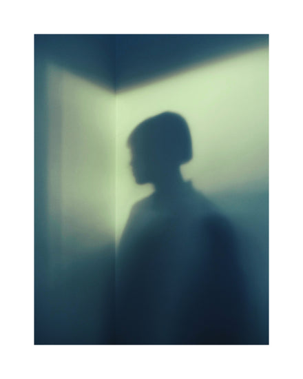 Shadow of a woman with short hair in the corner of a room with white walls.
