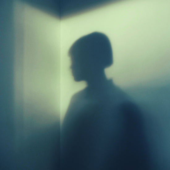 Shadow of a woman with short hair in the corner of a room with white walls.