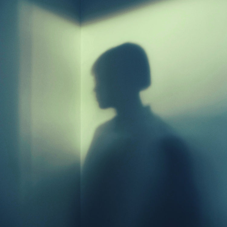 Shadow of a woman with short hair in the corner of a room with white walls.