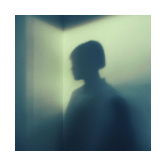 Shadow of a woman with short hair in the corner of a room with white walls.