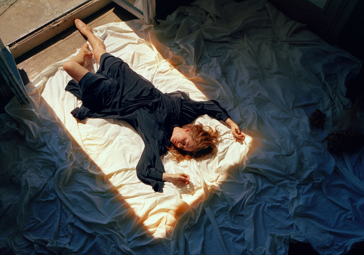 Woman in a blue dress laying in the sun coming in through an open door.